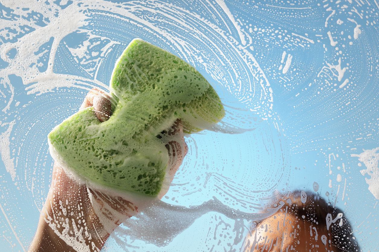 Window cleaner using a sponge to wash a window with clear blue sky