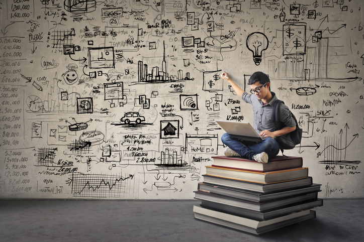 Young man sitting on books drawing creative ideas while looking at computer